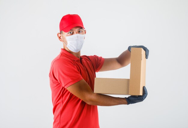 Livreur en uniforme rouge, masque médical, gants tenant une boîte en carton ouverte