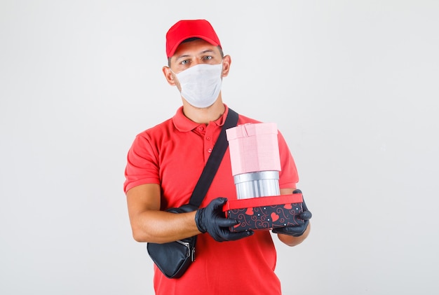 Livreur en uniforme rouge, masque médical, gants tenant des boîtes présentes