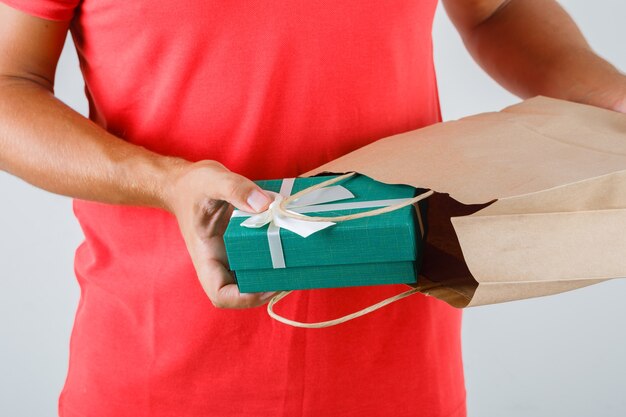 Livreur en uniforme rouge prenant présent fort hors de sac en papier