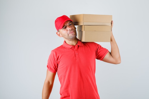 Livreur en uniforme rouge tenant des boîtes en carton sur son épaule et à mécontent