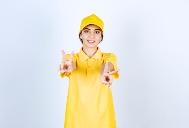 Livreuse en uniforme jaune debout et montrant le signe de la victoire.