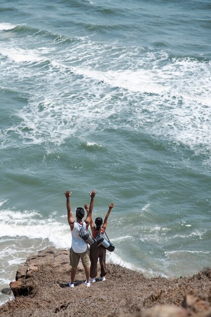 Long shot couple avec les mains en l'air au bord de la mer