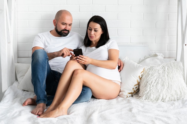 Long Shot Heureux Couple Vérifiant Le Téléphone Pour Les Noms De Bébé