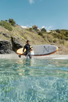 Long shot homme tenant une planche de surf