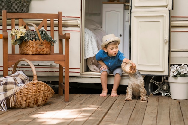 Long shot petit garçon assis sur une caravane à côté d'un chien mignon