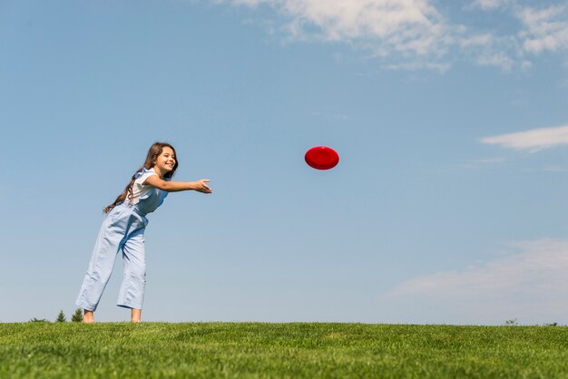 Long shot petite fille jouant avec un frisbee rouge