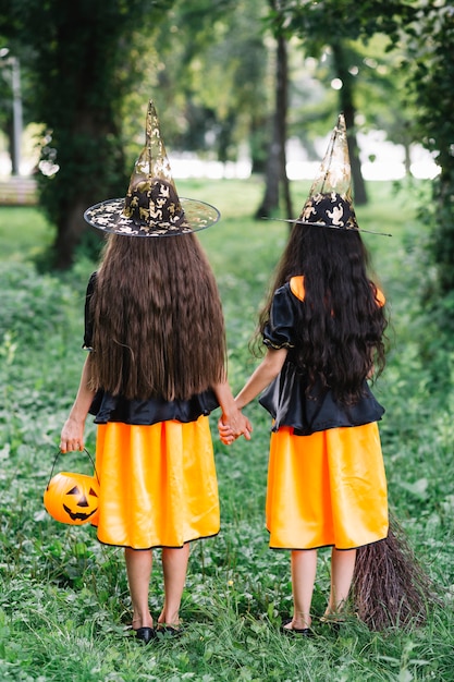 De longues filles aux cheveux en costumes de sorcière tenant par la main