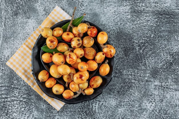 Loquats dans un bol sur un tissu et fond texturé gris. vue de dessus. espace pour le texte