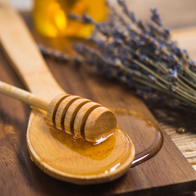 Louche de miel sur une cuillère en bois avec du miel sur une planche à découper