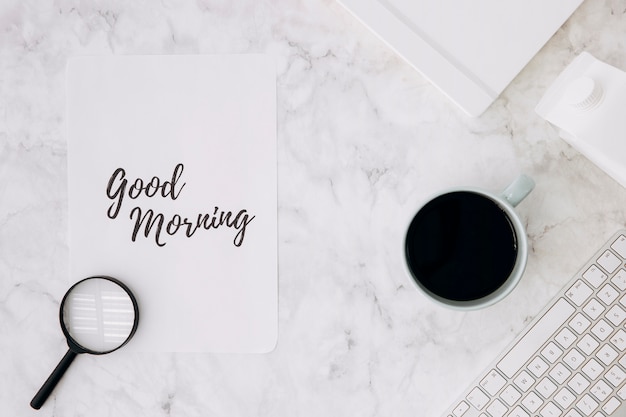 Loupe sur bon matin papier avec une tasse de café; agenda et clavier sur bureau en marbre blanc