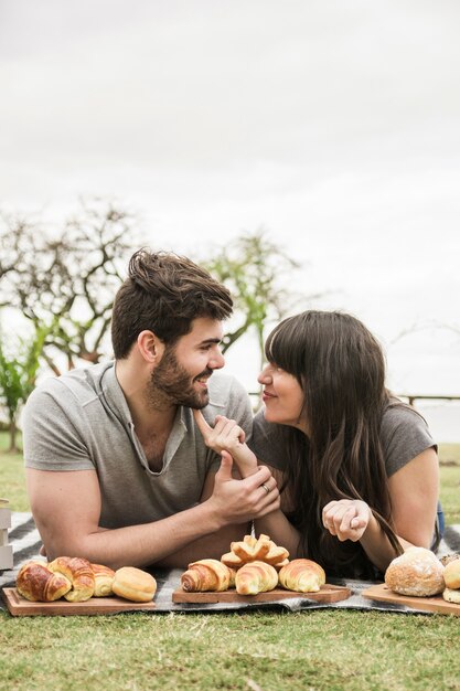 Loving jeune couple allongé sur une couverture avec des aliments cuits au four dans le parc