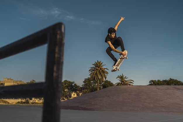 Low angle shot of a man skateboarding dans un skatepark vide avec des arbres et un ciel