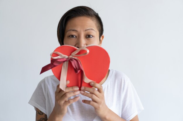 Ludique femme tenant une boîte cadeau en forme de coeur devant la bouche