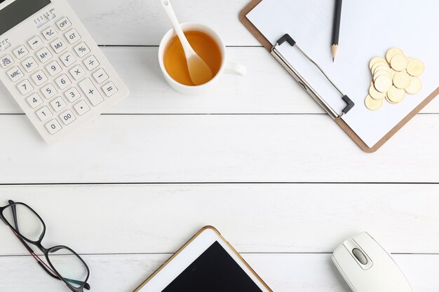 Lunettes, calculatrice, pièces de monnaie et tablette sur blanc bureau soigné