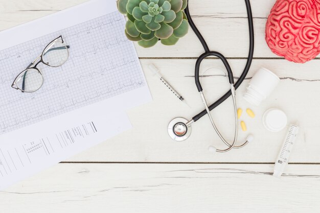 Lunettes sur électrocardiogramme; plante de cactus; stéthoscope; des pilules; seringue sur le bureau