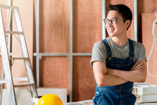 Des lunettes pratiques et attrayantes, un artisan masculin asiatique ou un architecte d'intérieur, se concentrent sur le travail du bois sur le site de construction, le concept de rénovation et d'amélioration de la conception intérieure de la maison