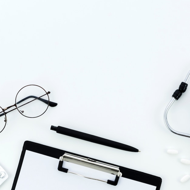 Lunettes; stylo; presse-papiers; pilules et stéthoscope sur fond blanc