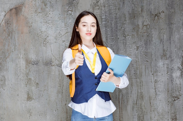 Lycéenne avec sac à dos jaune et dossier donnant les pouces vers le haut. Photo de haute qualité