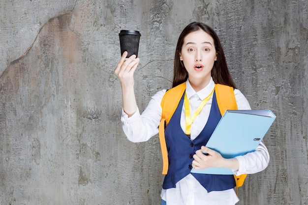 Lycéenne tenant une tasse de café et un dossier. Photo de haute qualité