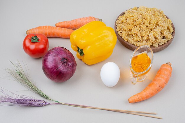 Macaroni cru aux légumes et oeuf sur une surface blanche