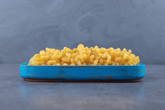 Macaroni cru de coude sur la plaque bleue.