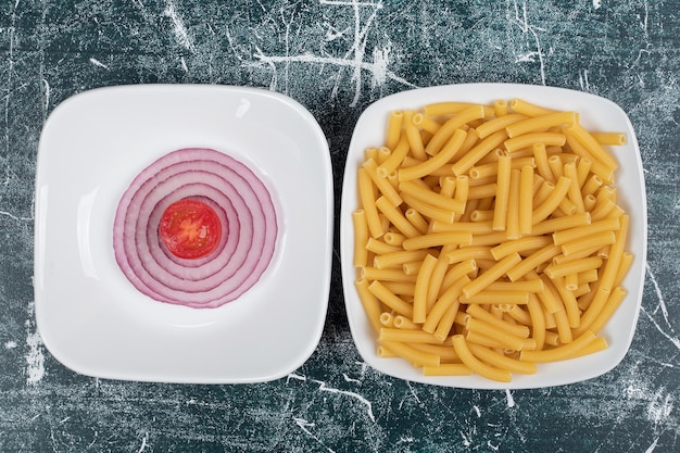 Photo gratuite macaroni frais non préparés avec des tranches d'oignon et de tomate cerise.