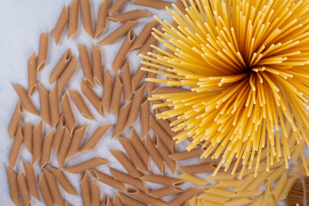 Macaroni non cuit avec des pâtes crues fraîches sur une surface blanche