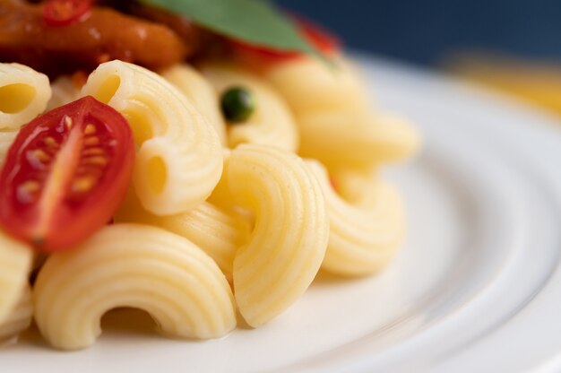 Macaroni sauté à la tomate, au piment, aux graines de poivre et au basilic dans un plat blanc.