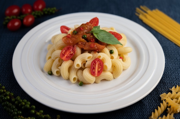 Macaroni sauté à la tomate, au piment, aux graines de poivre et au basilic dans un plat blanc.