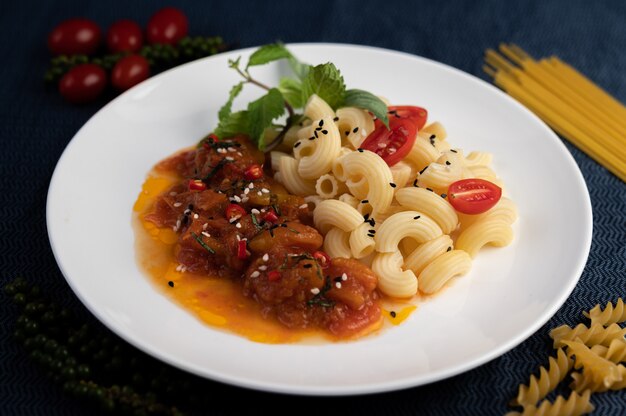 Macaroni sauté à la tomate, au piment, aux graines de poivre et au basilic dans un plat blanc.