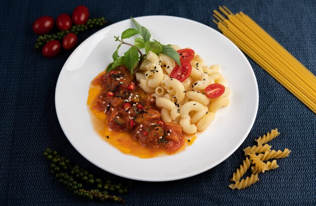 Macaroni sauté à la tomate, au piment, aux graines de poivre et au basilic dans un plat blanc.