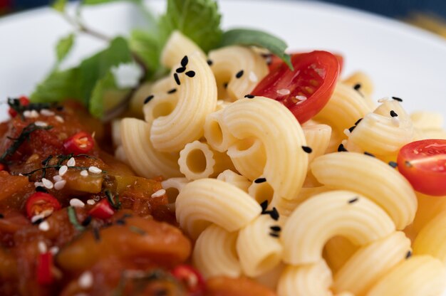 Macaroni sauté à la tomate, au piment, aux graines de poivre et au basilic dans un plat blanc.