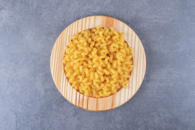 Macaroni sec cru sur plaque de bois.