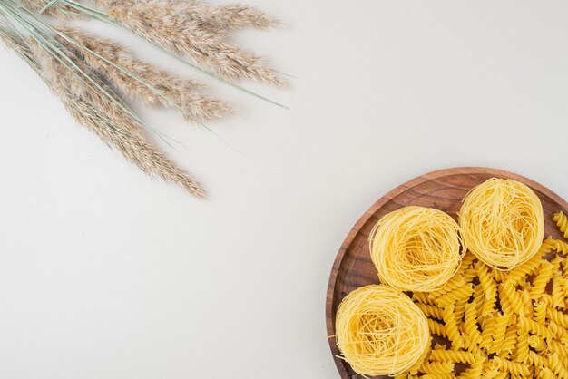 Macaroni et spaghettis en spirale crus sur plaque en bois