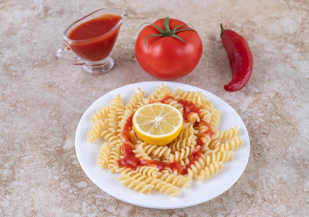 Macaroni avec un verre de ketchup et divers légumes sur une surface en marbre.