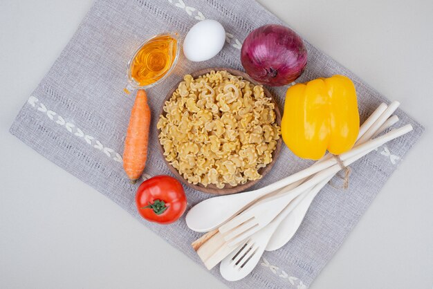 Macaronis crus aux légumes sur plaque en bois sur nappe