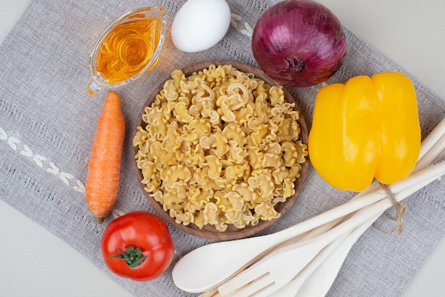 Macaronis crus aux légumes sur plaque en bois sur nappe