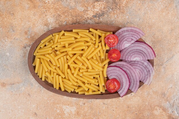 Macaronis frais non préparés avec des tranches d'oignon et de tomate cerise. Photo de haute qualité