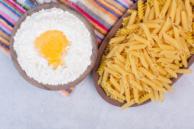 Macaronis non cuits sur des bols en bois avec du jaune et de la farine