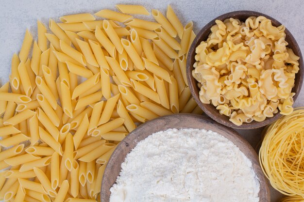 Macaronis non cuits sur des bols en bois avec du jaune et de la farine