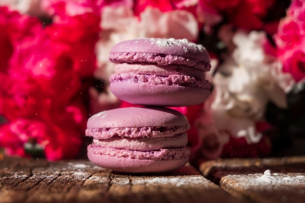 Macarons crémeux violets avec du sucre en poudre sur le bouquet de fleurs rose en bois