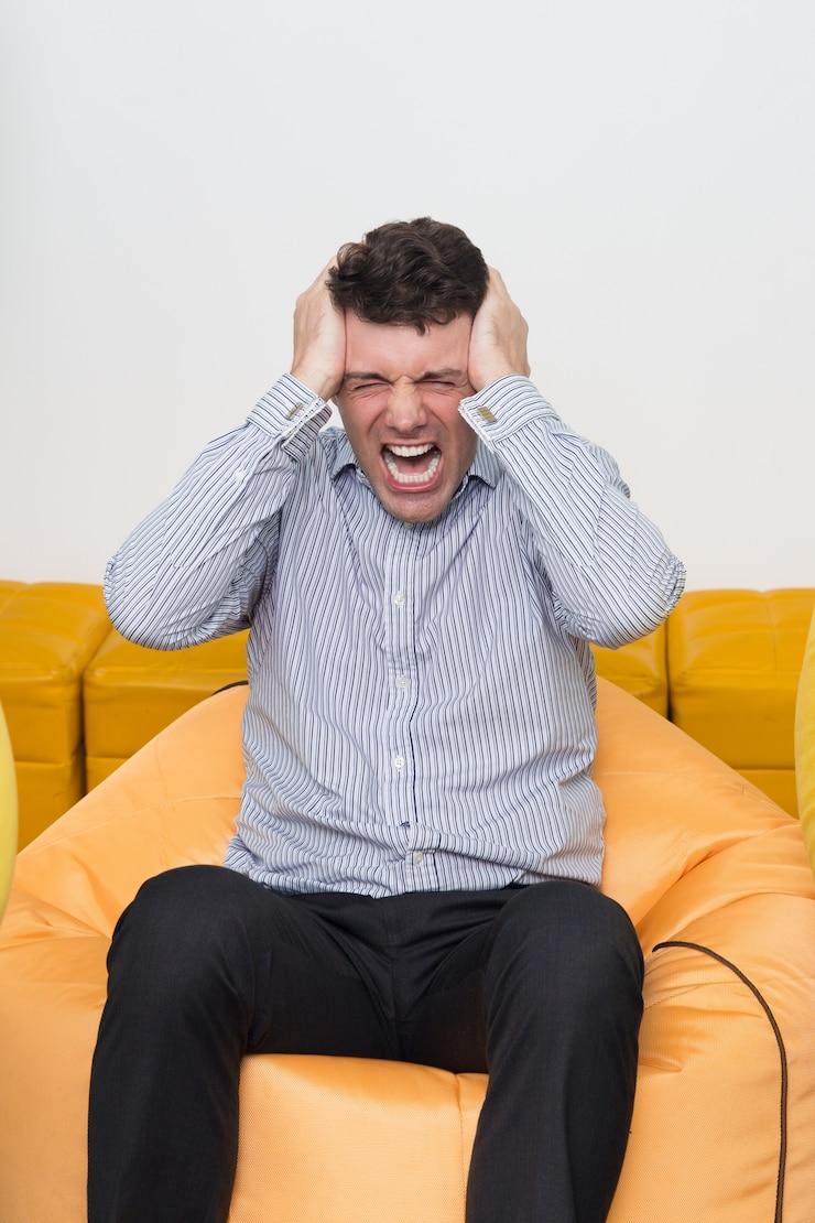 Photo gratuit mad jeune homme assis sur le pouf au bureau en pleurant