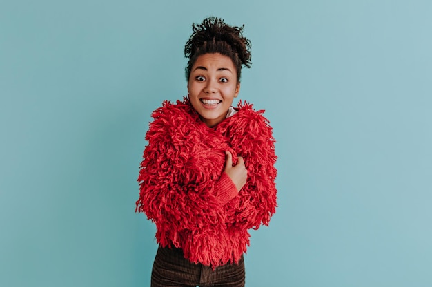 Magnifique femme afro-américaine posant dans une veste pelucheuse rouge Prise de vue en studio d'une jeune femme noire insouciante isolée sur fond turquoise