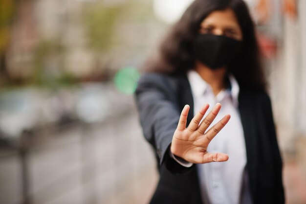 Une magnifique femme indienne porte un masque formel et noir posant dans la rue pendant la pandémie de covid Elle montre un panneau d'arrêt à la main