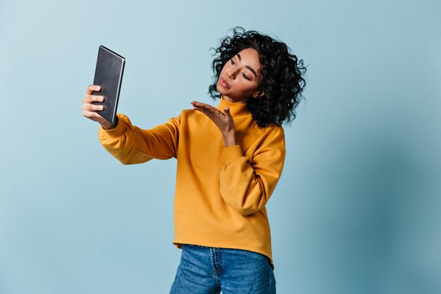 Magnifique fille envoyant un baiser aérien pendant un appel vidéo Femme adorable à l'aide d'une tablette numérique sur fond bleu