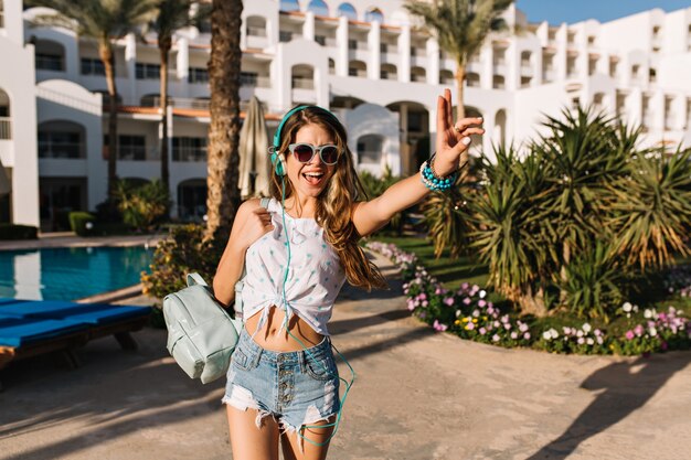 Magnifique fille mince à la peau de bronze regardant par-dessus son épaule en allant de l'hôtel à la plage de la mer.