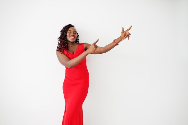 Magnifique jeune femme africaine en robe rouge luxueuse contre un mur blanc. beauté, mode. pointez le doigt vers le haut.