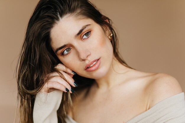 Magnifique jeune femme au maquillage léger. Pensive jolie fille posant sur un mur marron.