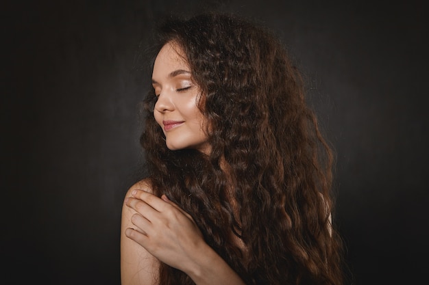 magnifique jeune mannequin européenne avec un maquillage soigné et une peau éclatante portant ses beaux cheveux noirs lâches, détournant les yeux avec un sourire joyeux, gardant les yeux fermés