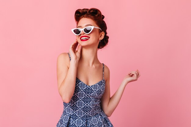 Magnifique pin-up posant dans des lunettes de soleil. Photo de Studio de femme au gingembre rêveuse isolée sur espace rose.